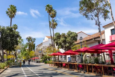 View of Santa Barbara, California street with neo-Spanish colonial architecture and wooden outdoor dining deck with tables and red umbrellas.