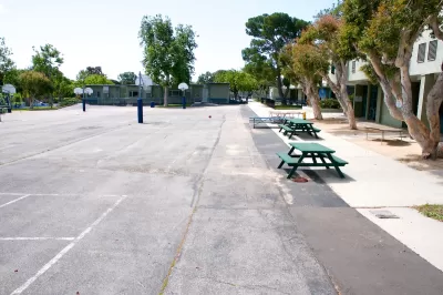 View of empty paved schoolyard with green picnic benches and basketball hoops in Malibu, California