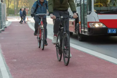 Two people on bikes in red painted bike lane with bus in traffic lane next to them.