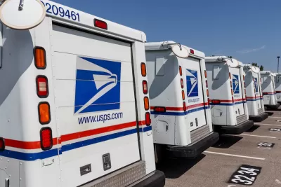 Row of USPS trucks parked in outdoor parking lot.