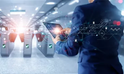 Man in suit holding tablet looking at subway turnstiles with superimposed graphics signaling technology and AI.