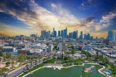 Aerial view of Macarthur Park lake with downtown Los Angeles skyline in background.
