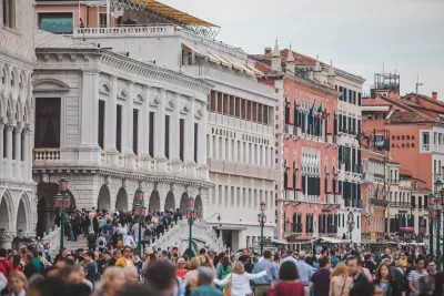 Line of colorful historic buildings on one side of a square jammed packed with people.