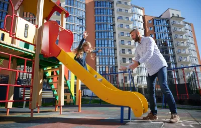 Man reaching for young girl sliding down playground slide.