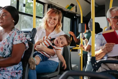 Woma holding small boy on lap sitting on public bus with many other passengers around them.