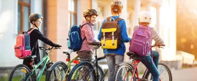 Group of four children with backpacks and helmets riding and walking their bikes.