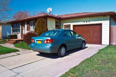 Blue small sedan in driveway of ranch-style one-story home with light green walls and dark brown garage door and trim.