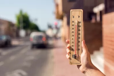Close-up of hand holding up wooden thermometer in front of blurred street