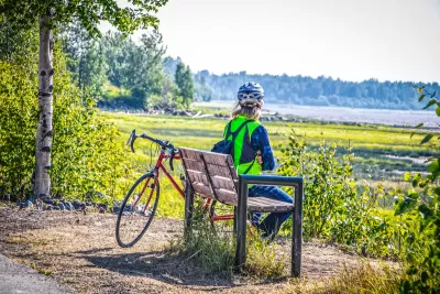 Cyclist in helmet sitting on bech looking out at lake and forest in Anchorage, Alaska.