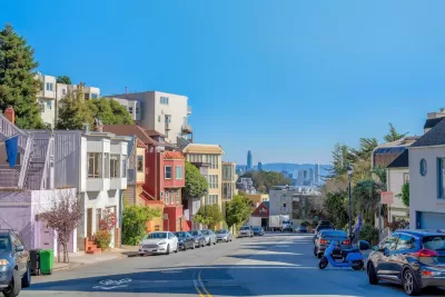 View down San Francisco street with colorful residential buildings and high-rise downtown buildings in distance.