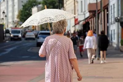 Older woman walking on city street holding white lace sun parasol.