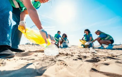People at beach on sunny day doing clean-up of plastic bottles and other trash.