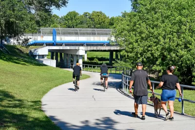 Concrete bike and pedestrian trail with people walking and biking under pedestrian bridge in Orlando, Florida.