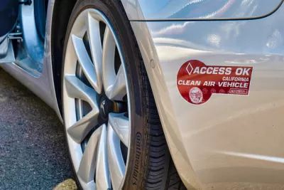 Close-up of maroon California 'Clean Air Vehicle' carpool lane access sticker on the back bumper of a silver Tesla vehicle.