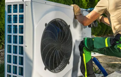 Close-up of worker installing white electric heat pump outdoors.