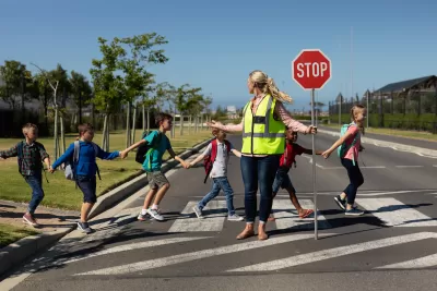 Group of children crossing a street with a crossing guard holding up red Stop sign.