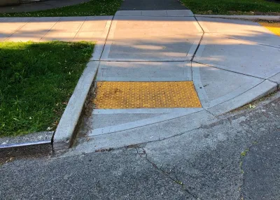 Curb cut at corner of sidewalk with yellow panel with bumps to indicate wheelchair ramp.