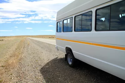White microbus with yellow stripe on rural road with empty road and blue sky in background.