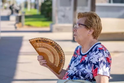 Older woman with short hair fanning herself with wood hand-held fan outdoors during hot afternoon