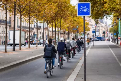 People on bikes ride on protected bike path along the Seine River in Paris, France