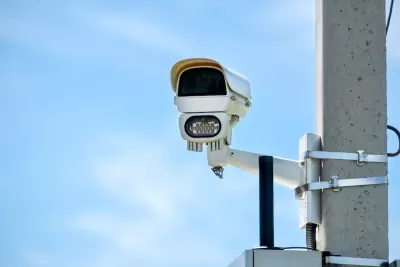 Close-up of white traffic enforcement camera mounted on concrete pole against blue sky.