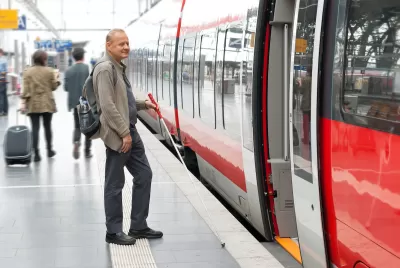 Man using cane for visual impairment waiting to board subway train on platform.