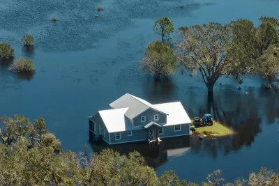 A gray hope with white roof surrounded by floodwaters that come up just above the home's foundations.