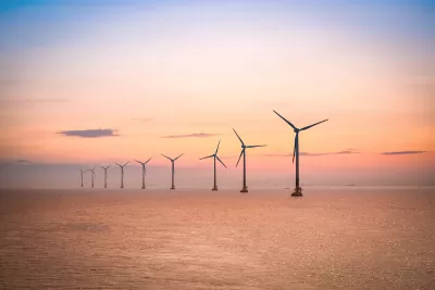 Row of offshore wind turbines in large water body against sunrise or sunset sky.