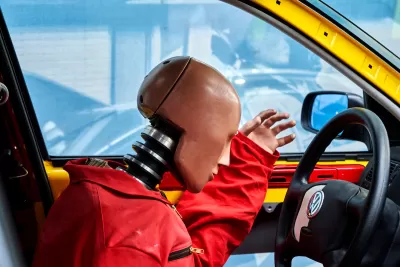 Close-up of crash test dummy in orange jumpsuit leaning over steering wheel with Volkswagen logo.