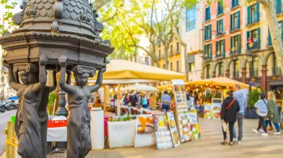Close-up of decorative water fountain on La Rambla pedestrian street in Barcelona, Spain with blurred pedestrians in background.