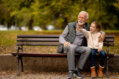 Grandfather and young girl sitting on park bench.