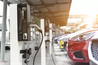 Close-up of red car parked and plugged in at EV charging station with row of cars behind it.