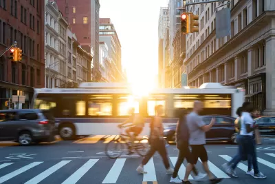 People, cars, bikes and buses traveling through a busy intersection on 5th Avenue and 23rd Street in New York City with shining sunlight background.