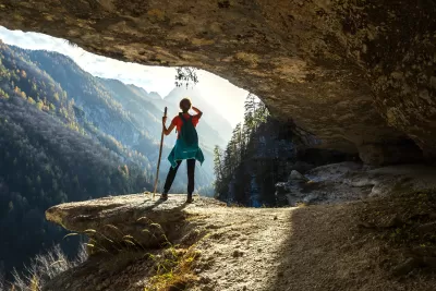 Woman stands on rock overlooking mountain valley.