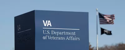 Close-up of Department of Veterans Affairs sign in Washington, D.C. with American and MIA flags on flagpole in background.