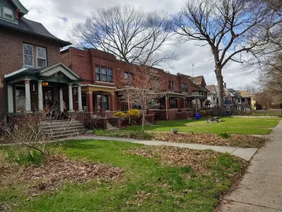 Row of older brick houses in Detroit with front porches and front lawns.