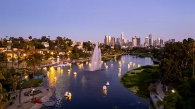 View from above of swan-shaped paddleboats with lights on around artesian fountain in Echo Park Lake with downtown Los Angeles skylien in background at twilight.