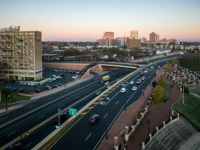 Overhead view of highway with offramps leading to overpass and buildings in the distance.