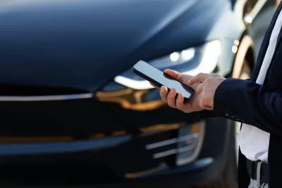 Close-up of hand holding smartphone and Tesla car hood in background.