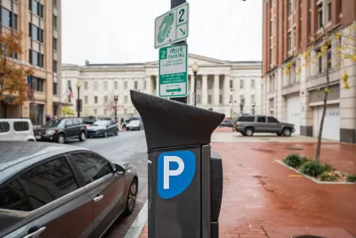 Electronic parking pay station next to curb in Washington D.C., on rain-soaked red brick sidewalk with neoclassical white building in background