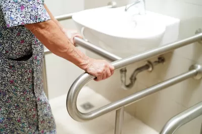 Close-up of woman in flowered dress holding bar next to white porcelain sink in bathroom.