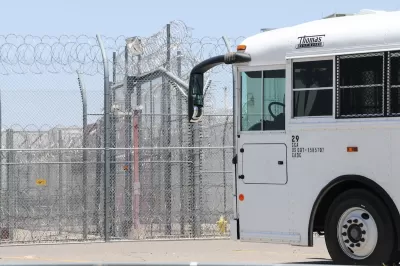 White prison transport bus passing in front of heavily fortified prison fence with barbed wire.