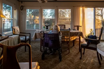 Senior woman sitting inchair looking out large window at golden hour in Broomes Island, Maryland.