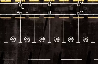 Overhead view of black asphalt parking lot with white lined parking spots with EV charging logos.