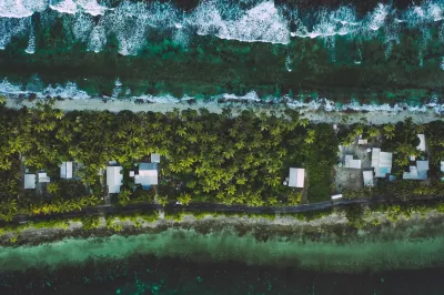 Bird's eye view of thin strip of land with palapas and palm trees in Tuvalu.