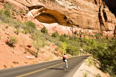 Person on bike wearing helmet biking on asphalt road with red cliffs in background in Zion National Park