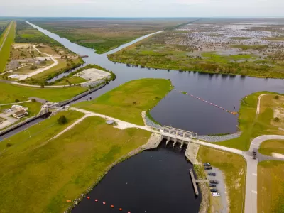 An aerial view of a lock and dam between two waterways with miles of marshes into the background of the image.