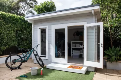 Small gray backyard cottage with glass door and bike sitting in front of it
