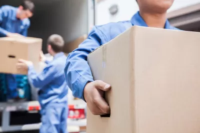 Blurred close-up of movers in blue coveralls unloading cardboard boxes from moving van.