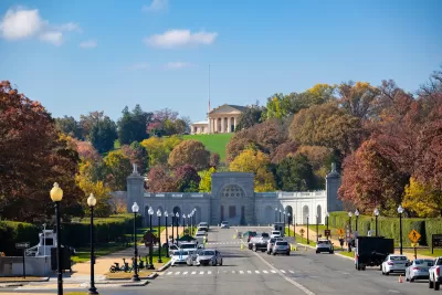 View of street in front of Arlington National Cemetery with ornate neoclassical building on hilltop in background.